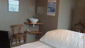 A hotel room with a bed, a wooden chair, a small table with a sink, and a poster on the wall.