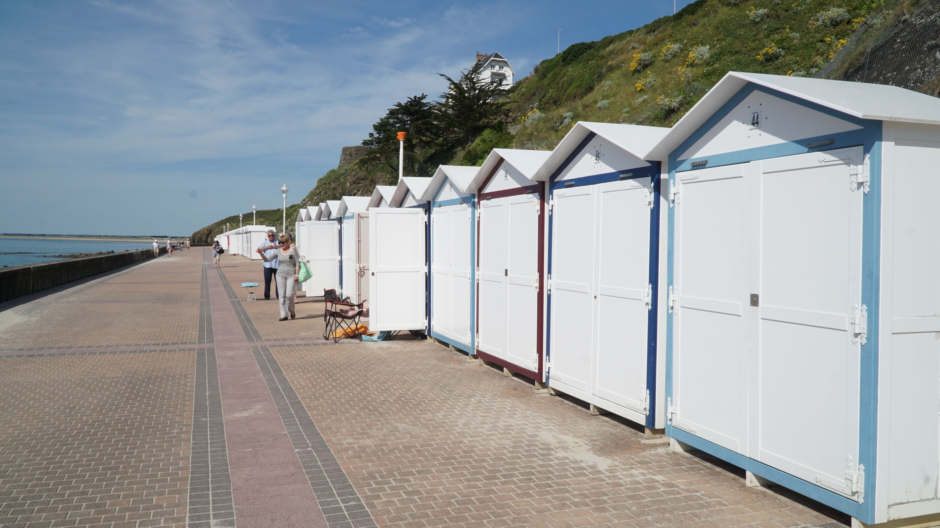 Une rangée de petits chalets situés en bord de mer, reliés à la plage par une promenade dallée.