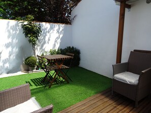 Eine Terrasse mit Kunstrasen, einem Holztisch, Stühlen und Kübelpflanzen.
