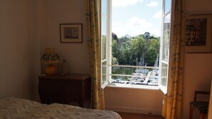 Ein Schlafzimmer mit Bett, Nachttisch, Lampe, einem Fenster mit Vorhängen und Blick auf eine Marina.