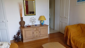 Ein Zimmer mit Holzboden, Holzschrank, Bett mit orangefarbener Decke, Nachttisch, Lampe, Vase und Spiegel an der Wand.