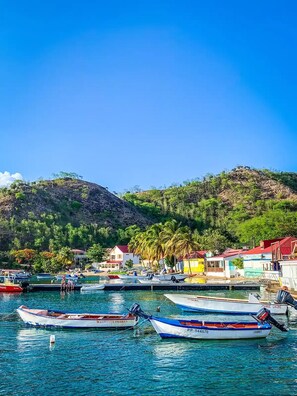 A coastal village with boats docked at a pier, surrounded by lush greenery and hills.