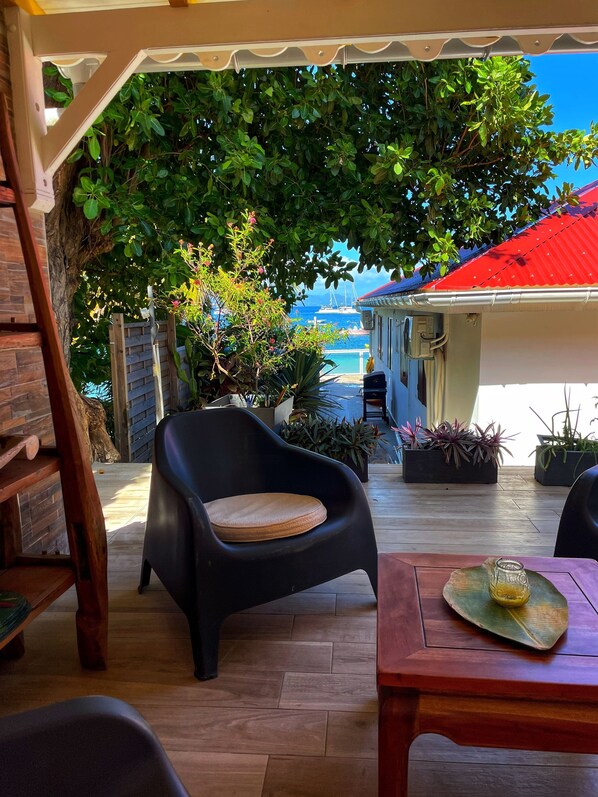 An outdoor seating area with a view of the sea, wooden furniture, and potted plants.