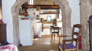 Cocina rústica con un arco que conduce a un comedor, que incluye un refrigerador, armarios de madera y varios utensilios de cocina.