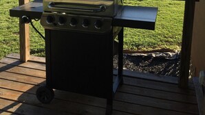 Una parrilla portátil sobre una terraza de madera, con un campo de césped y árboles al fondo.