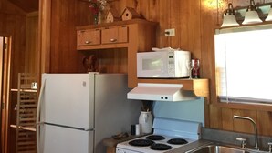 Una cocina compacta con armarios de madera, un refrigerador blanco, un microondas, una estufa y un lavamanos.