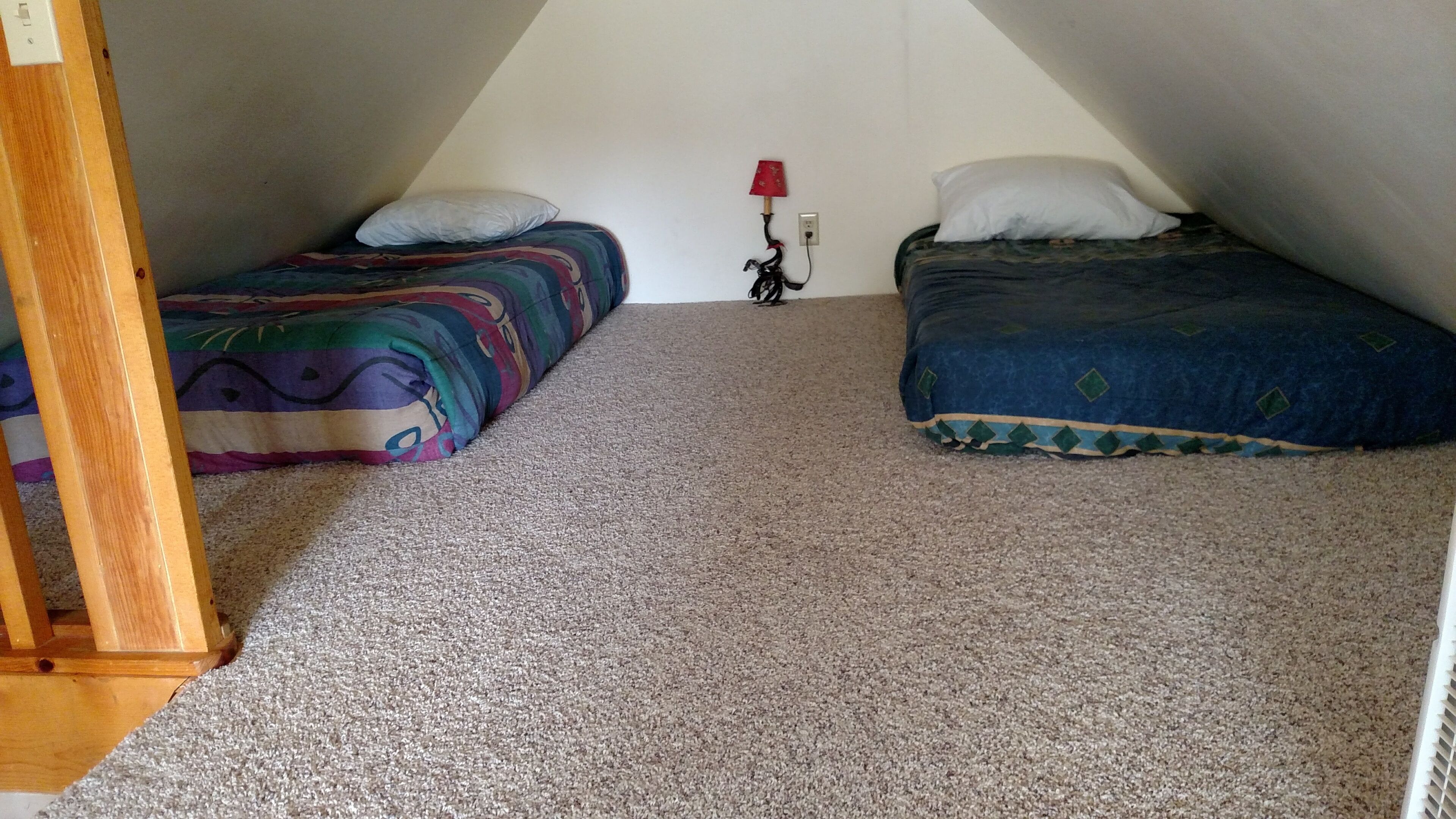 Ein kleines, dreieckiges Schlafzimmer im Dachgeschoss mit zwei Betten, einer roten Lampe und einem Holzstuhl.