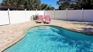 A swimming pool with clear blue water, surrounded by a white fence, and two red and white striped chairs. - Dream holiday at a low price: huge travel discounts now available! (Fort Myers)