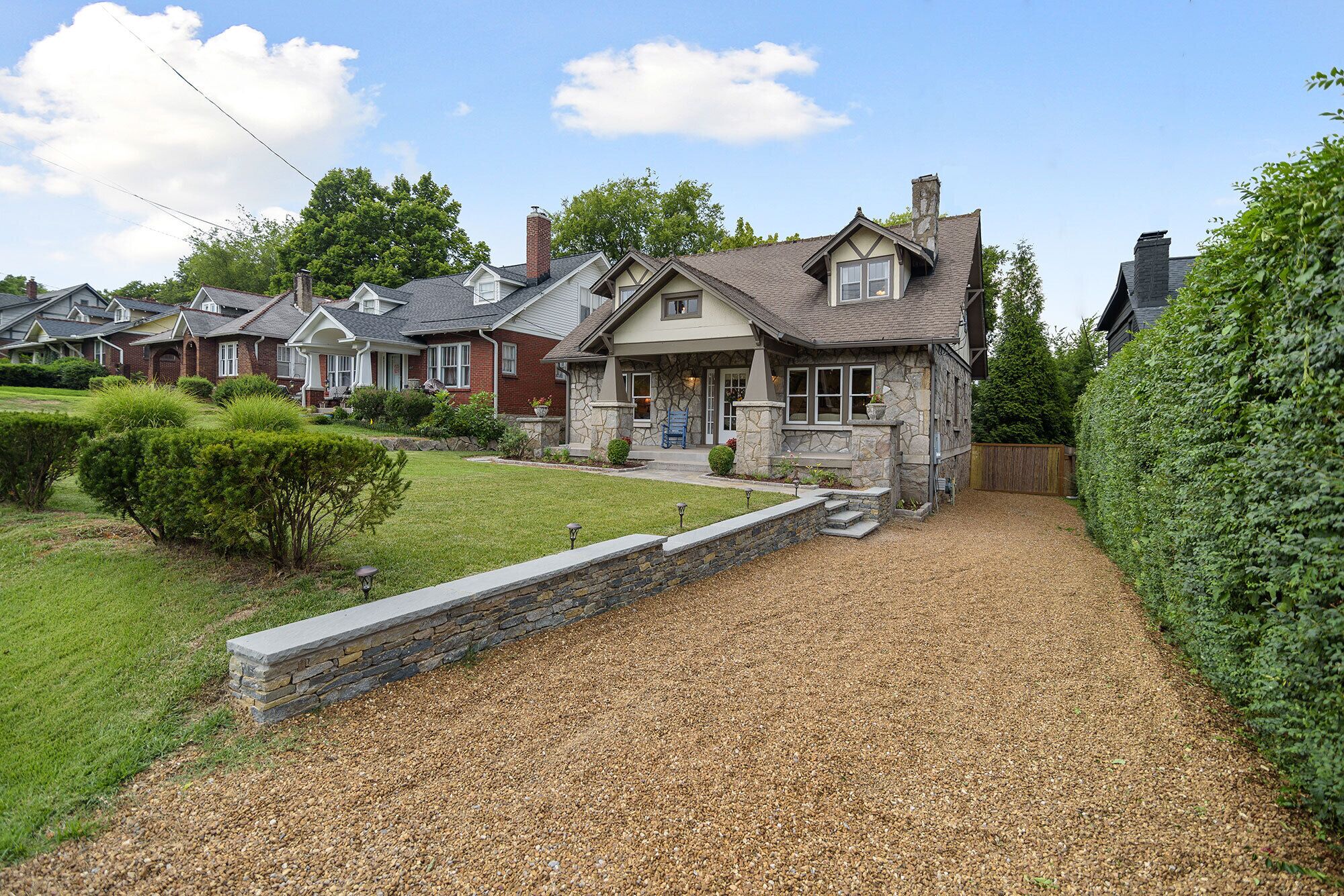 A residential house with a stone facade, a front porch, and a gravel driveway.