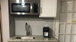 Una cocina con gabinetes blancos, microondas de acero inoxidable, un lavamanos y una cafetera.