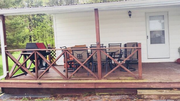 Un patio exterior techado con una mesa, sillas, una parrilla y una terraza de madera.