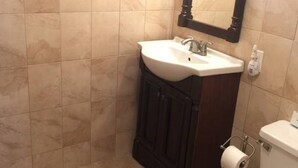 Un baño con lavamanos blanco, mueble de madera oscura y un inodoro.