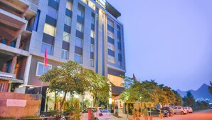 Un hotel de varios pisos con un letrero llamativo, balcones y un estacionamiento con automóviles.