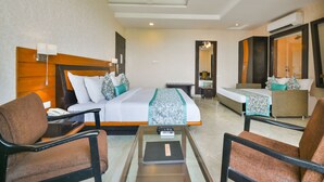 Habitación de hotel con una cama grande, dos sillones, una mesita, un escritorio, un espejo y un ventilador de techo.