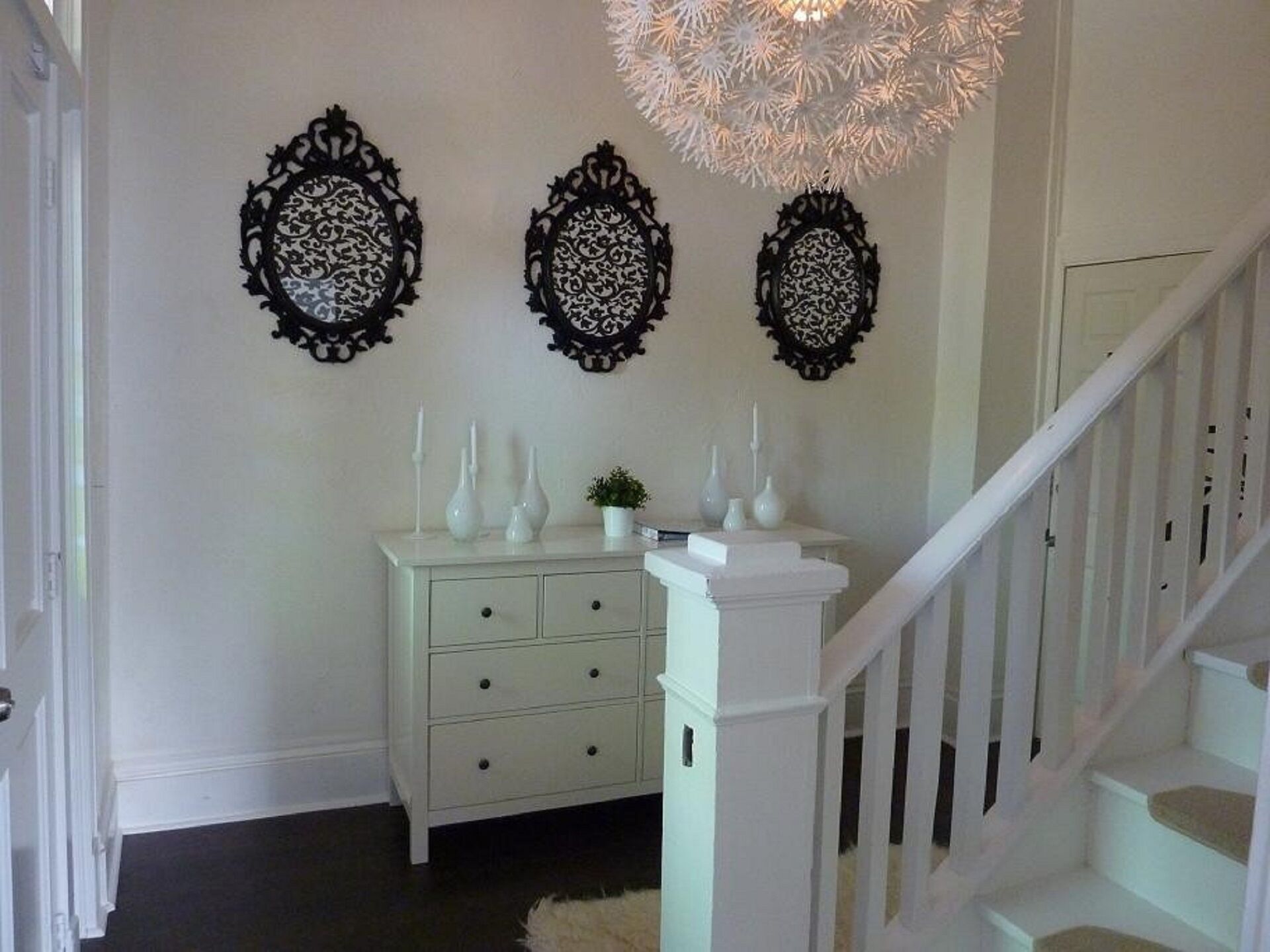 Una escalera con barandilla blanca y una pared blanca decorada con tres elementos ornamentales negros.
