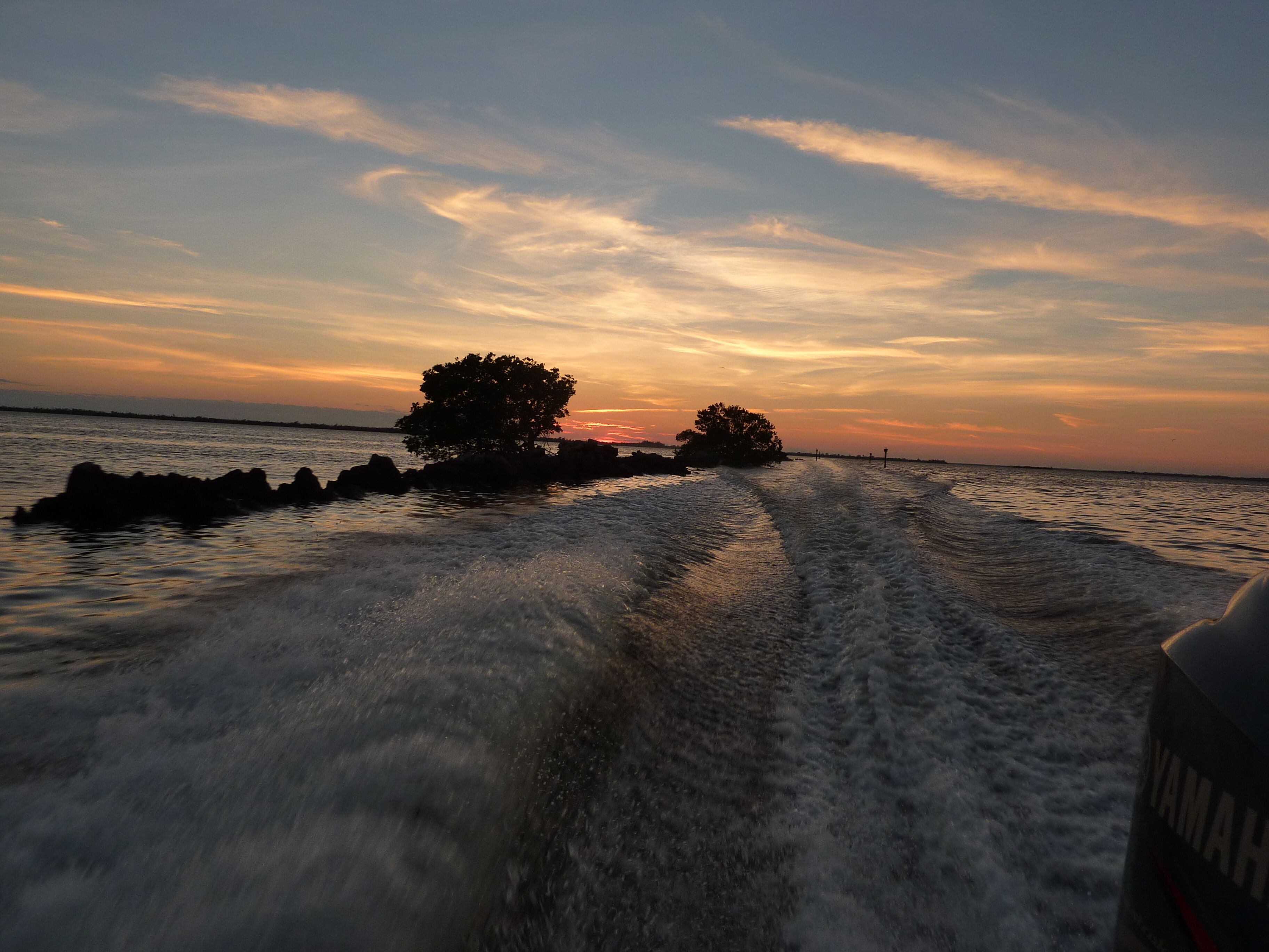 Una estela de barco en el agua, con un atardecer de fondo.