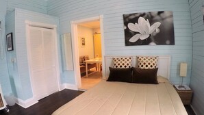 Un dormitorio con una cama, una mesita de noche, un cuadro colgado en la pared y una puerta que da a otra habitación.
