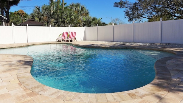Una piscina con borde curvo, rodeada por una valla blanca y una pequeña bandera estadounidense.