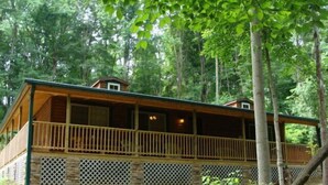 A cabin with a wooden deck and stone foundation, surrounded by trees.