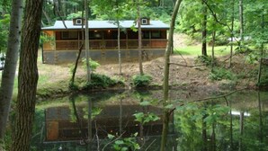 A cabin with a deck, surrounded by trees and a pond.
