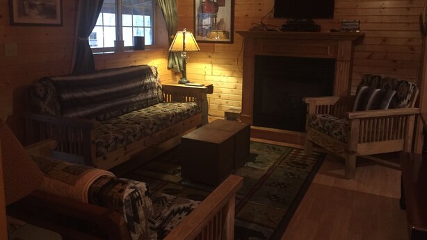 A cozy log cabin interior with a sofa, armchair, fireplace, and a television.