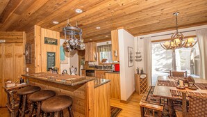 Un interno in legno con isola della cucina, sgabelli da bar, un tavolo da pranzo con sedie e un lampadario.