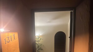 Une porte avec le numéro « 1311 » inscrit sur le mur, une plante en pot, un tapis à rayures et un plancher en bois.