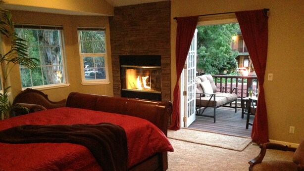 Une chambre dotée d’un grand lit, d’une cheminée, d’une vue sur l’extérieur et d’un balcon avec un fauteuil.