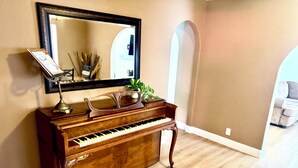 Un piano à queue dans une pièce au plancher en bois, avec un miroir au-dessus et une plante posée sur le piano.