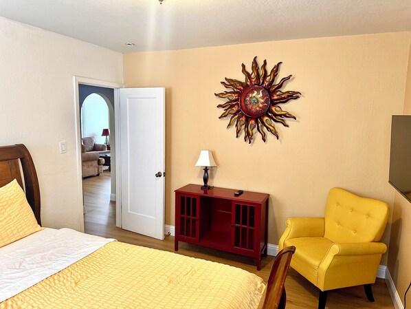 Ein Schlafzimmer mit einem Bett, einem gelben Sessel, einem roten Schrank und einem dekorativen Wandbild mit Sonnendecor.
