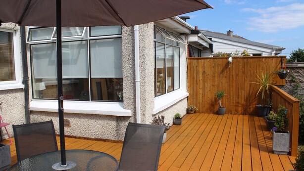 A wooden deck with a glass table and chairs, surrounded by potted plants and a wooden fence. - Cois Ba House (Dublin)