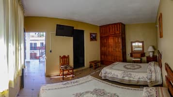 A bedroom with two beds, a wooden wardrobe, a chair, a small table, and a television mounted on the wall.