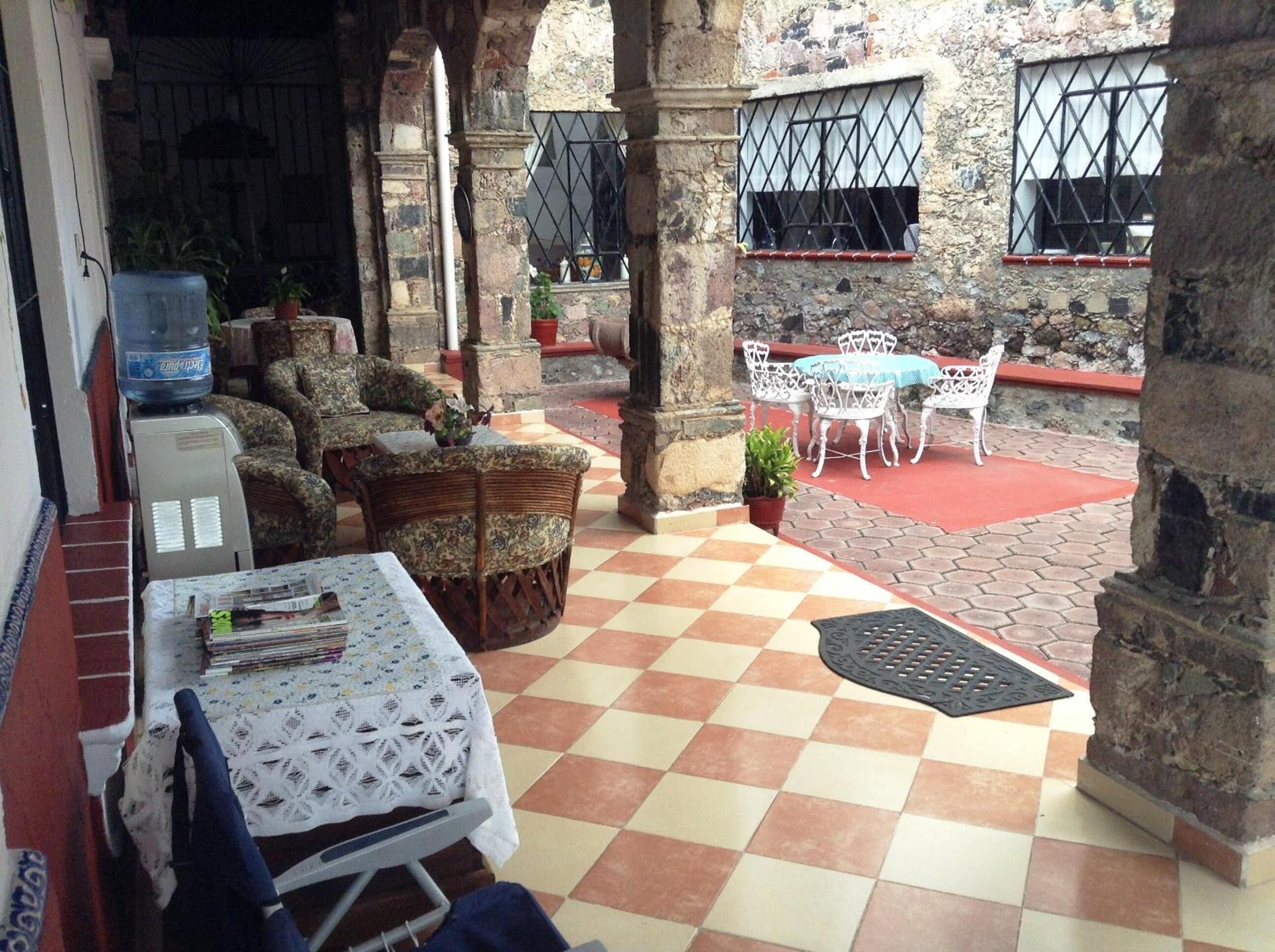 Un patio cubierto con suelo a cuadros, muebles de mimbre y una mesa con mantel de encaje.