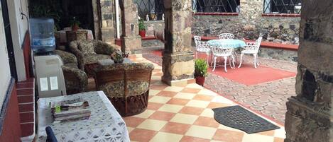 Un patio cubierto con suelo a cuadros, muebles de mimbre y una mesa con mantel de encaje.