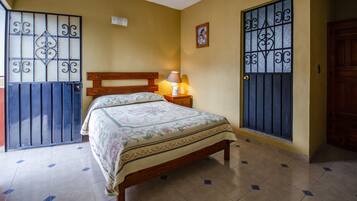 A bedroom with a bed, a nightstand, a lamp, a picture on the wall, and a door with a metal gate.