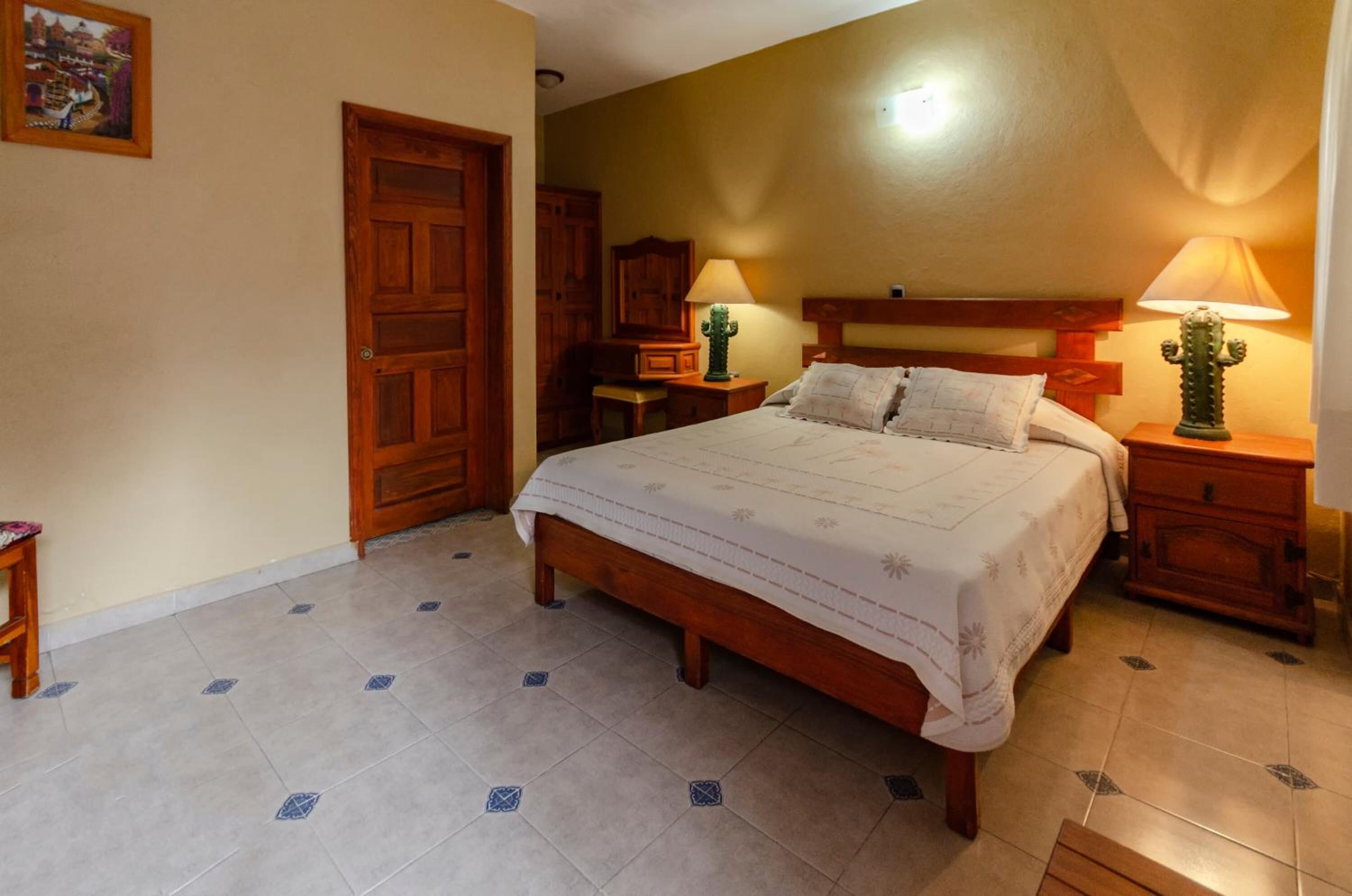 Une chambre à coucher avec un lit en bois, deux tables de chevet avec des lampes, une armoire en bois et une porte.