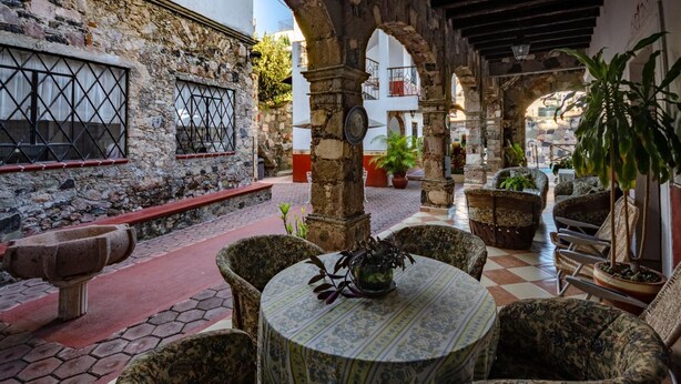 Un patio exterior con paredes de piedra, piso a cuadros y mobiliario de mimbre.
