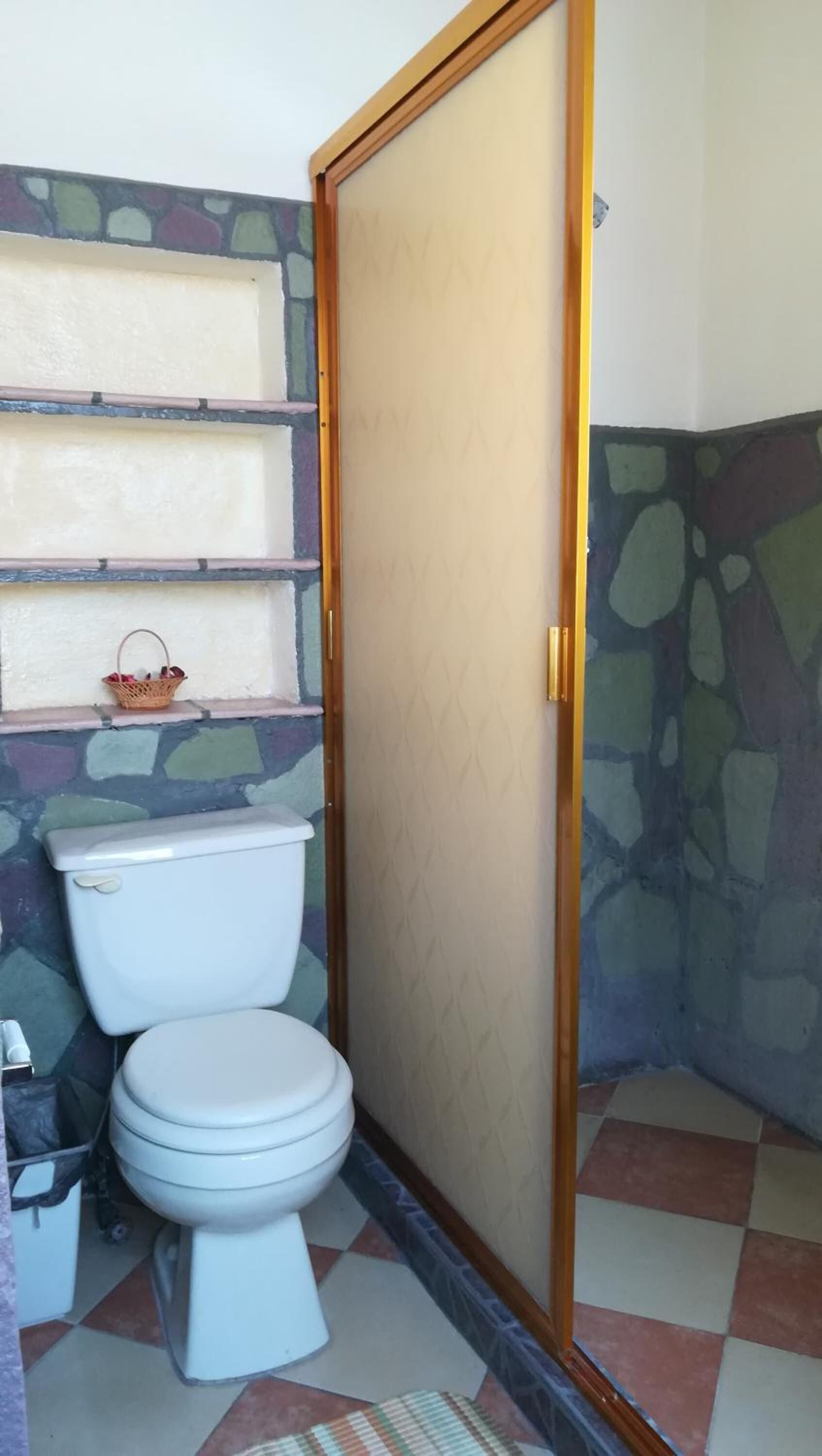 Un baño con inodoro, zona de ducha y un pequeño estante con una cesta.