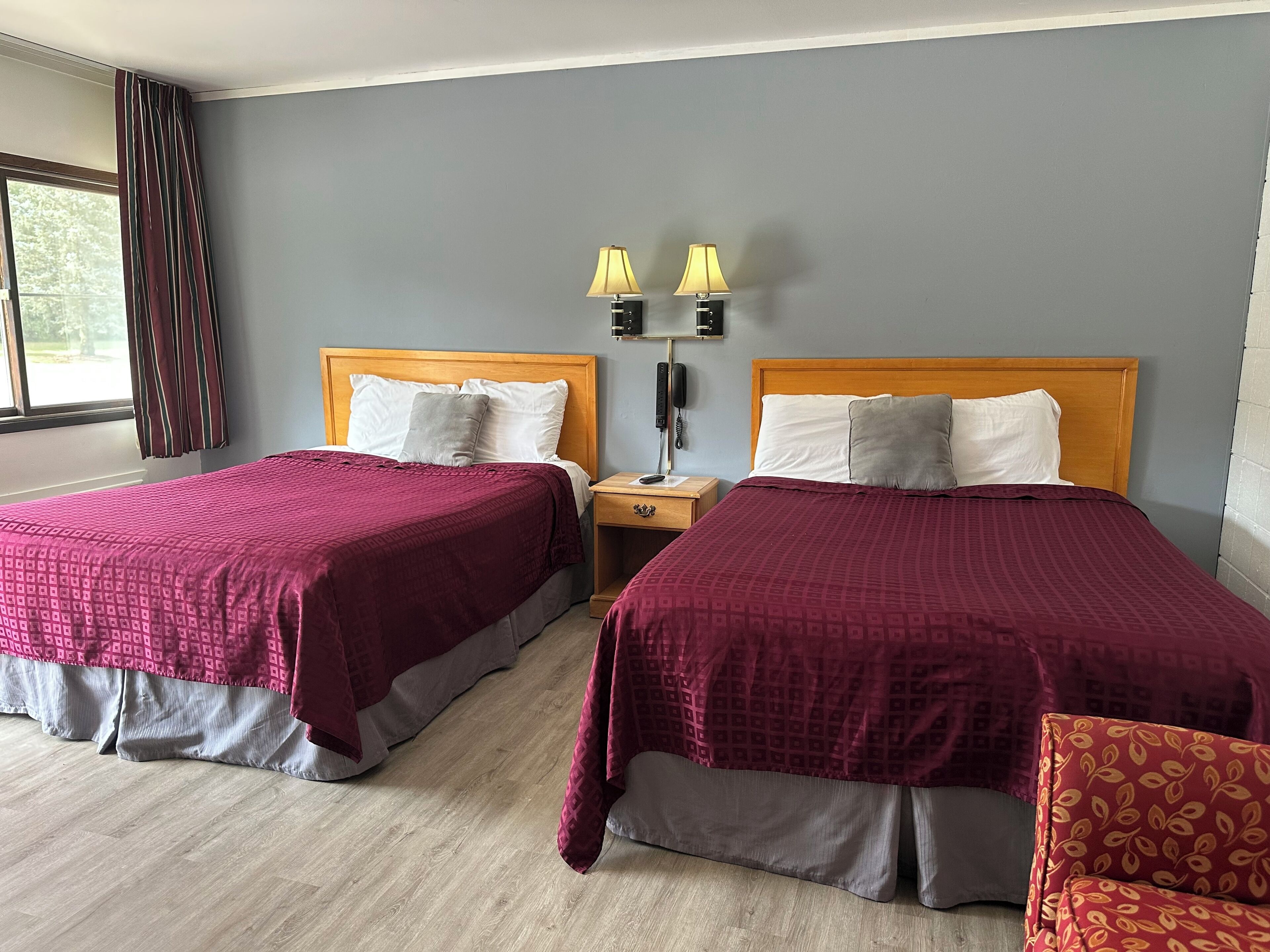 A hotel room with two beds, a nightstand with lamps, and a window with curtains.
