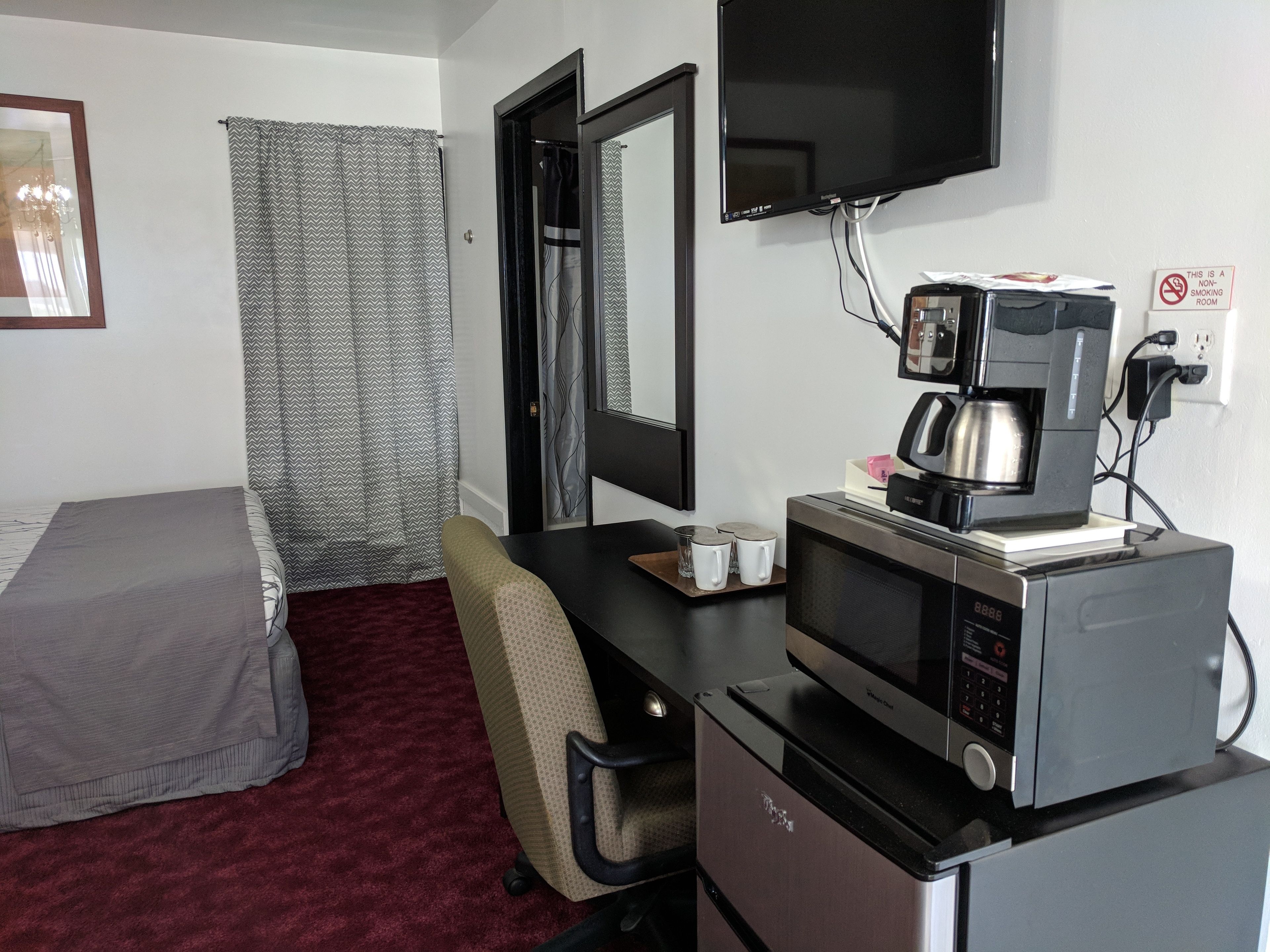A hotel room with a bed, a desk with a coffee maker, a TV, and a no-smoking sign.