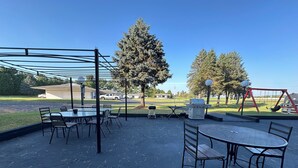 An outdoor patio area with tables and chairs, a barbecue grill, and a swing set. - Skyview Motel (Prairie du Sac)