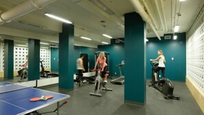 A gym with exercise equipment, a ping pong table, and teal walls. - Backpacker College at EC Vancouver: APT Living (Vancouver)