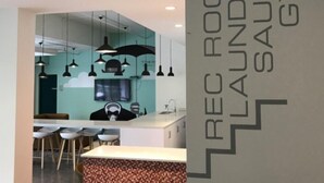 A modern interior with a reception area, a bar, and a visible sign indicating a rec room, laundry, sauna, and gym. - Backpacker College at EC Vancouver: APT Living (Vancouver)