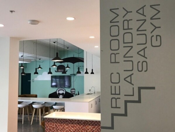 Un intérieur moderne comprenant un espace d’accueil, un bar et un panneau indiquant clairement la présence d’une salle de jeux, d’une buanderie, d’un sauna et d’une salle de sport.
