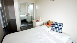 A hotel room with a large bed, a bedside table with a book and a candle, a mirror, and a door leading to another room. - Backpacker College at EC Vancouver: APT Living (Vancouver)
