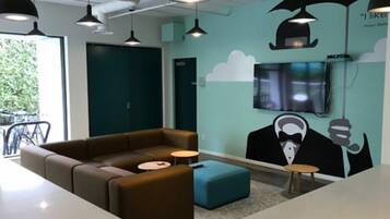 A modern lounge area with a brown sofa, a blue ottoman, and a flat-screen TV mounted on the wall.