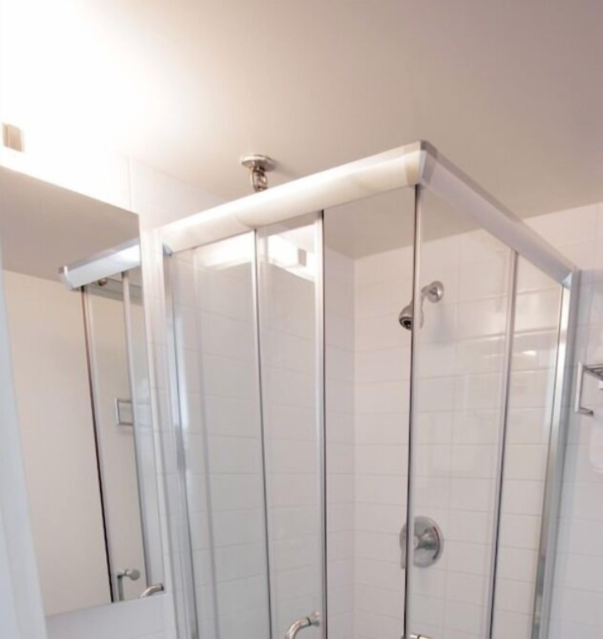 Ducha con cerramiento de vidrio, pared de azulejos blancos y cabezal de ducha cromado.