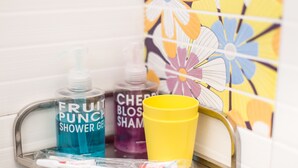 A bathroom sink with a tray holding a toothbrush, a blue bottle of Fruit Punch Shower Gel, and a yellow cup. - Safari Hotel (Kowloon)