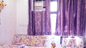 A hotel room with two beds, floral bedding, a small table with a vase of flowers, and purple curtains. - Safari Hotel (Kowloon)