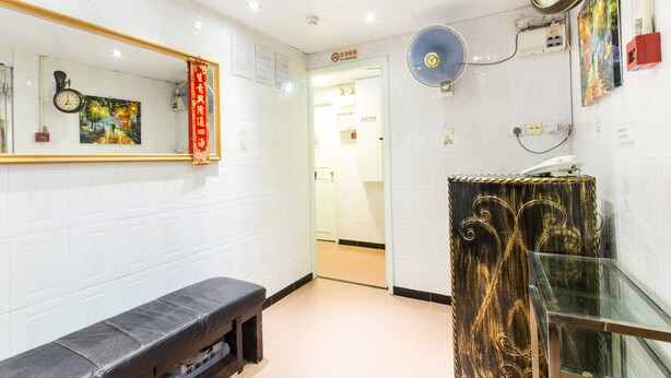 A hotel lobby with a bench, a clock, a fan, and a mirror on the wall. - Safari Hotel (Kowloon)